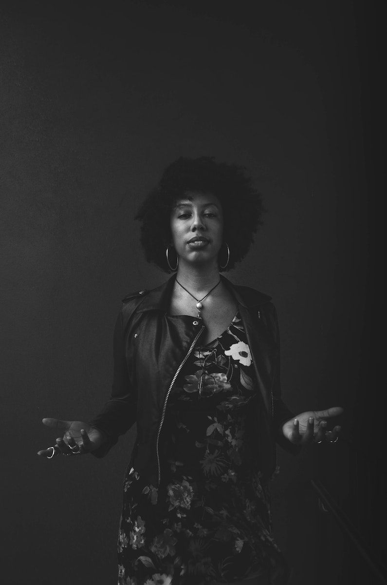 Serious black woman shrugging hands against dark background