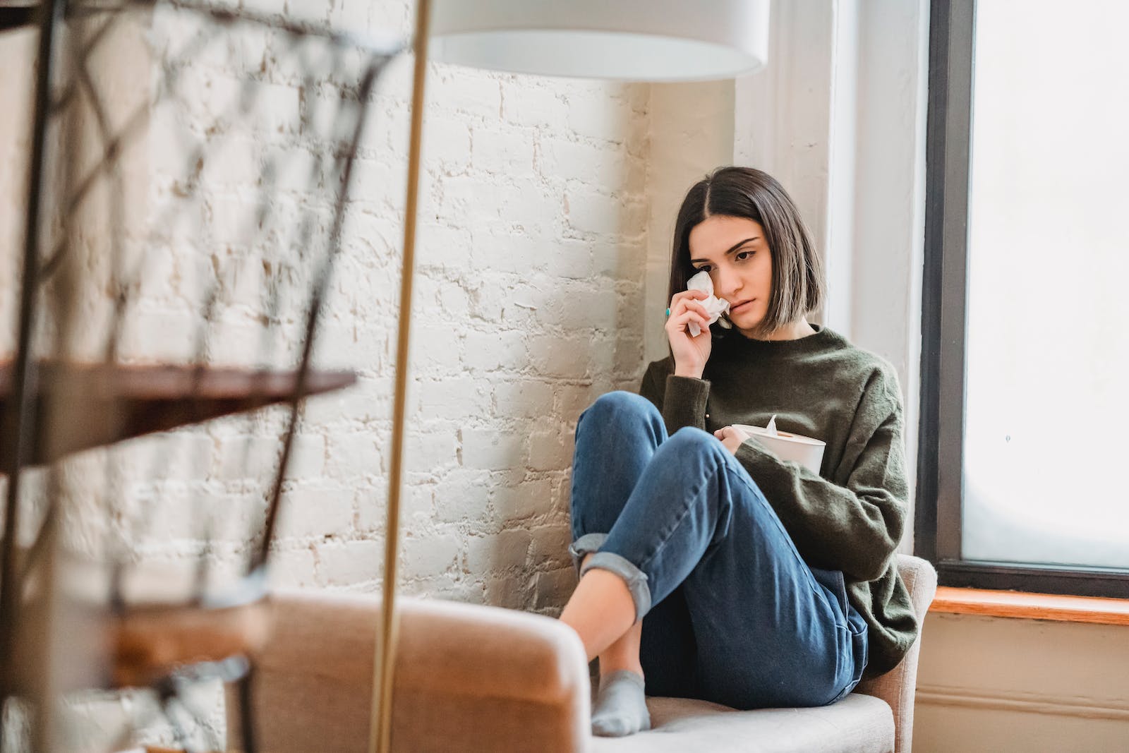 Desperate young ethnic female millennial crying on couch and wiping tears